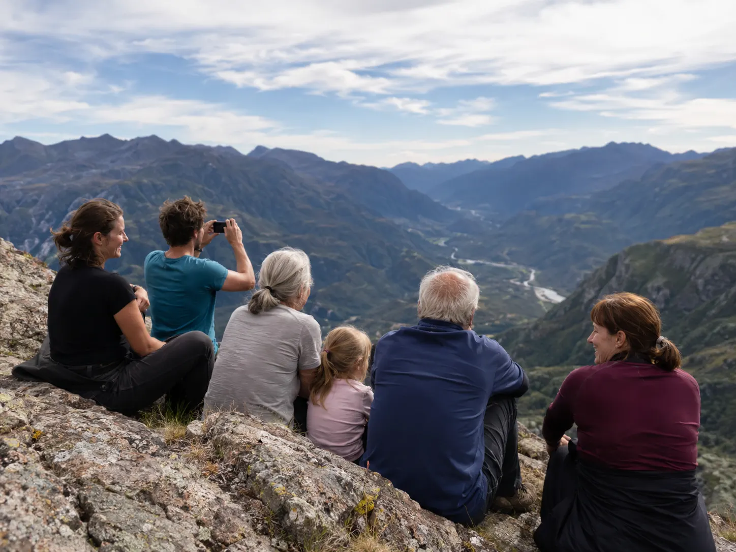 Mehrgenerationen-Familie auf einem felsigen Gipfel mit Blick ins Tal