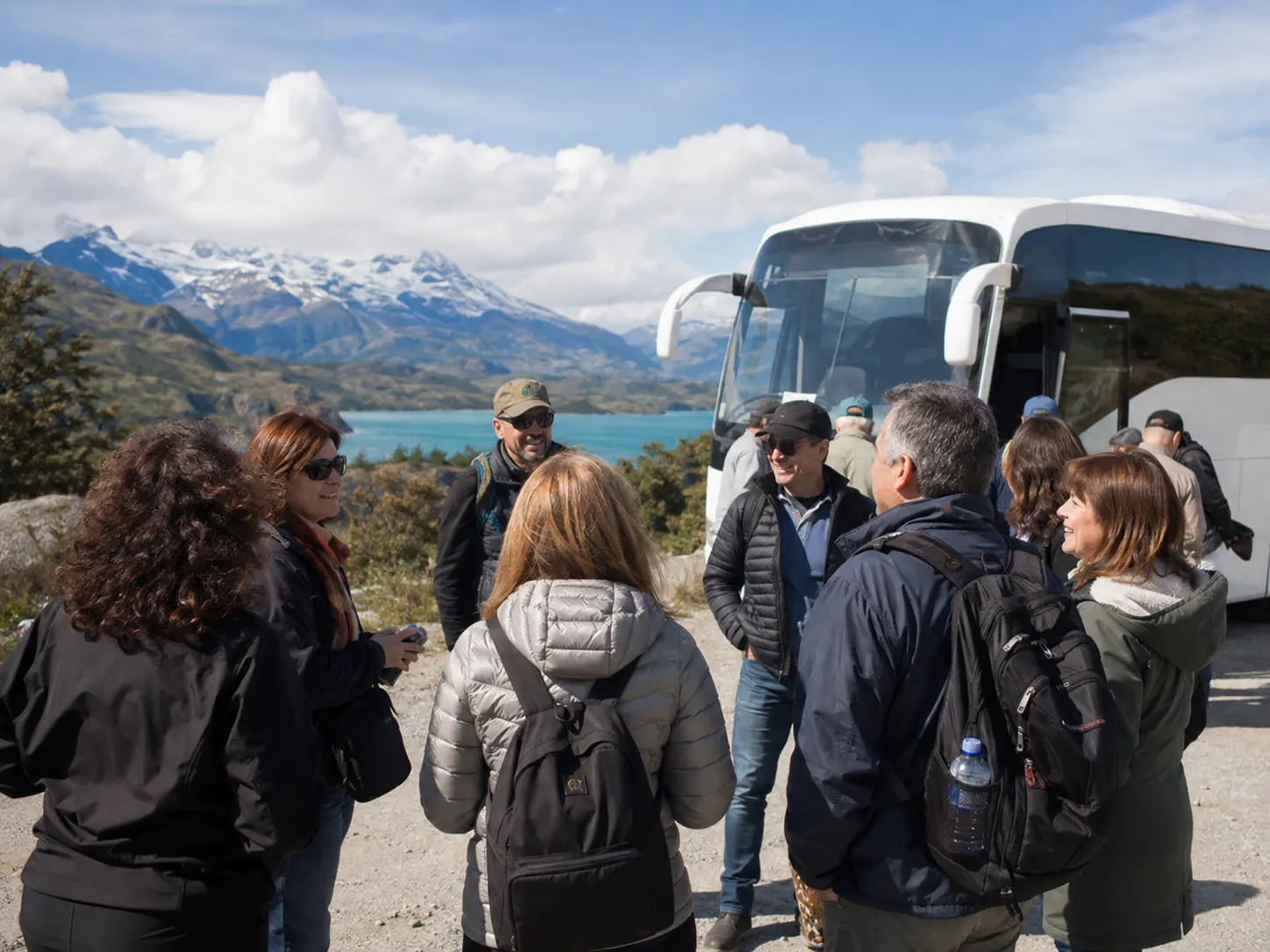 Reisegruppe mit Rucksäcken an einem Reisebus vor einer Seelandschaft